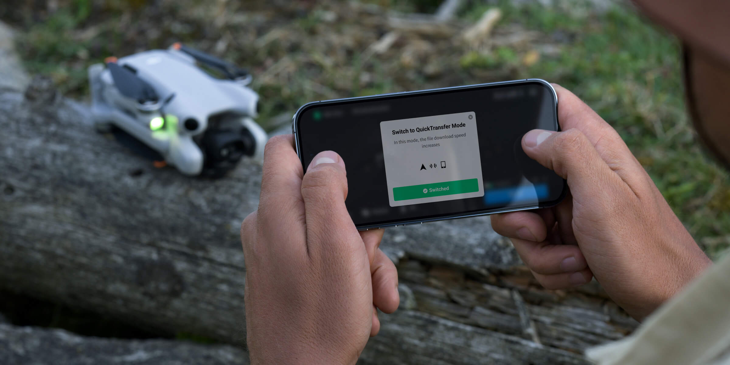 Foto de uma pessoa segurando seu smartphone com as duas mãos e ao fundo o DJI Mini 4 Pro