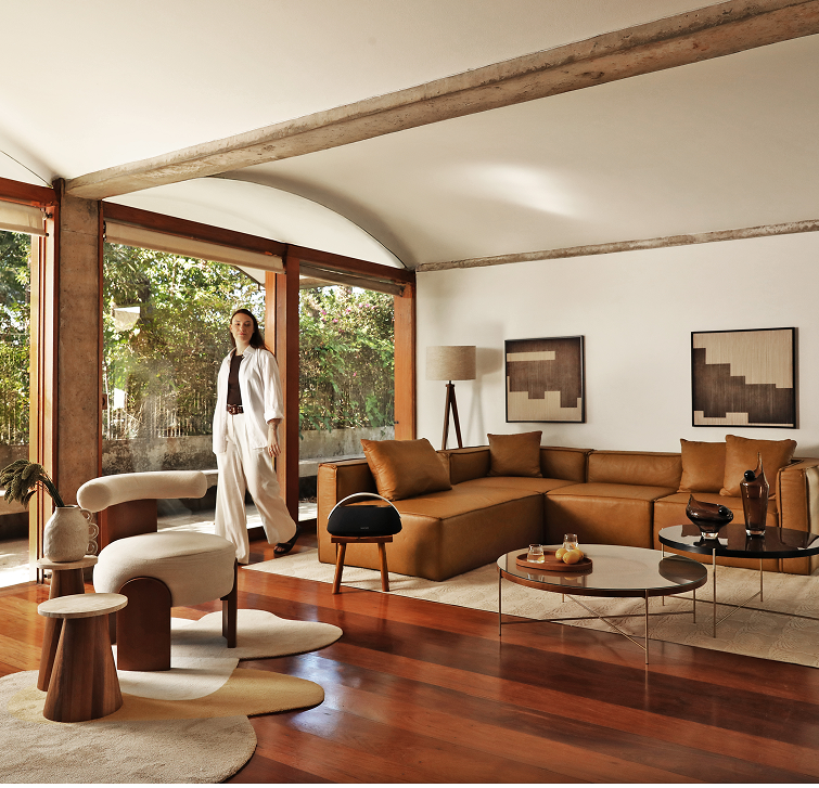 Quarto com cama arrumada, espelho de formato orgânico e um banco de design ao lado da cama.