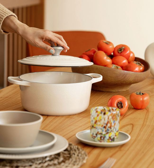 Mesa de jantar posta com panela de cerâmica branca, tigelas e tomates frescos.